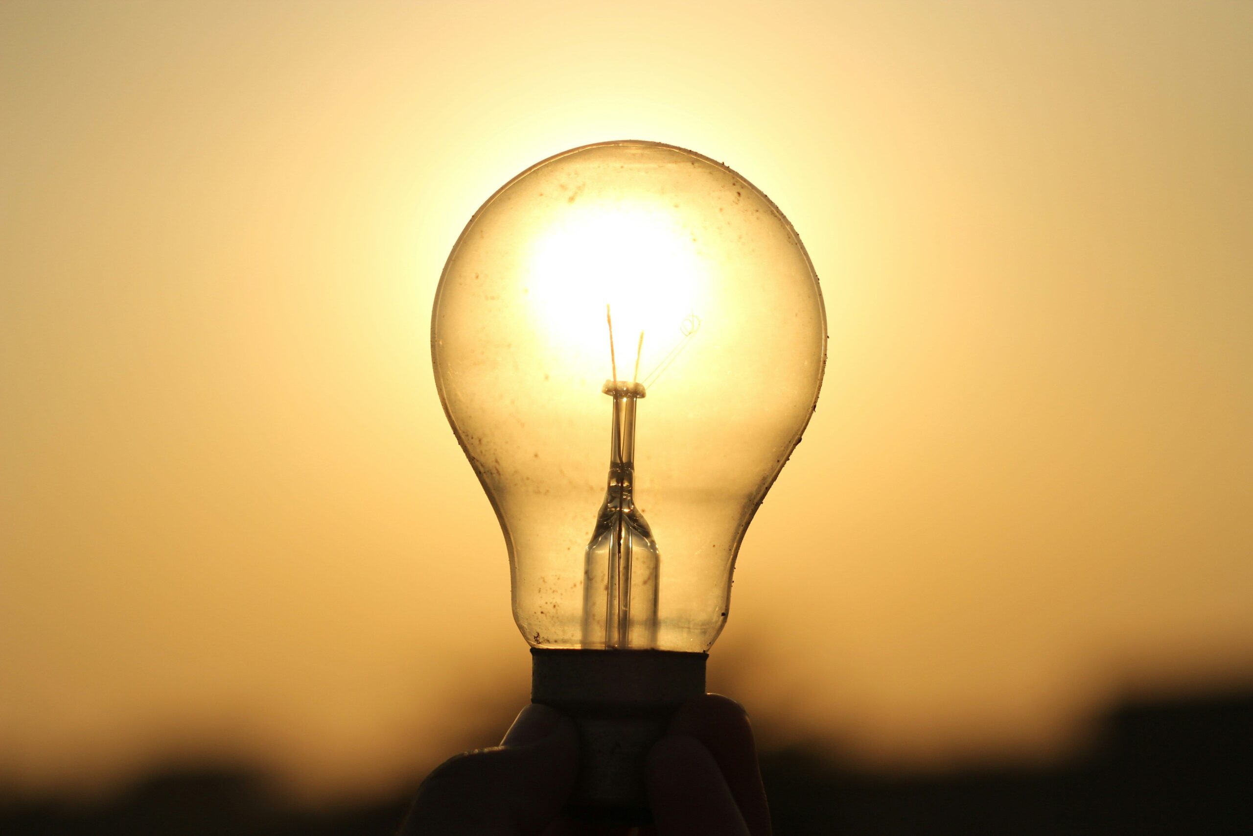 A light bulb held against a golden sunset in Lahore, symbolizing energy and innovation.